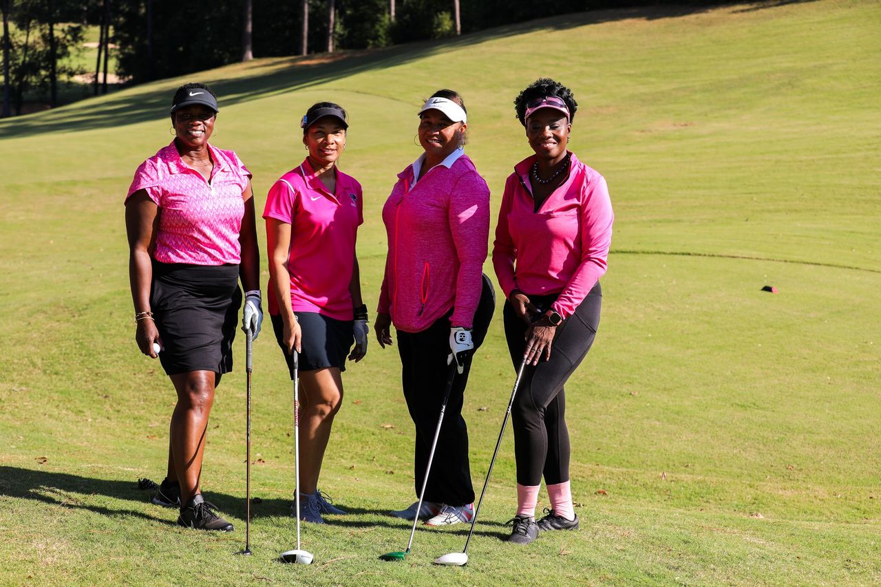 A group of four ladies pose for a photo with their golf clubs at the MTC Golf Classic