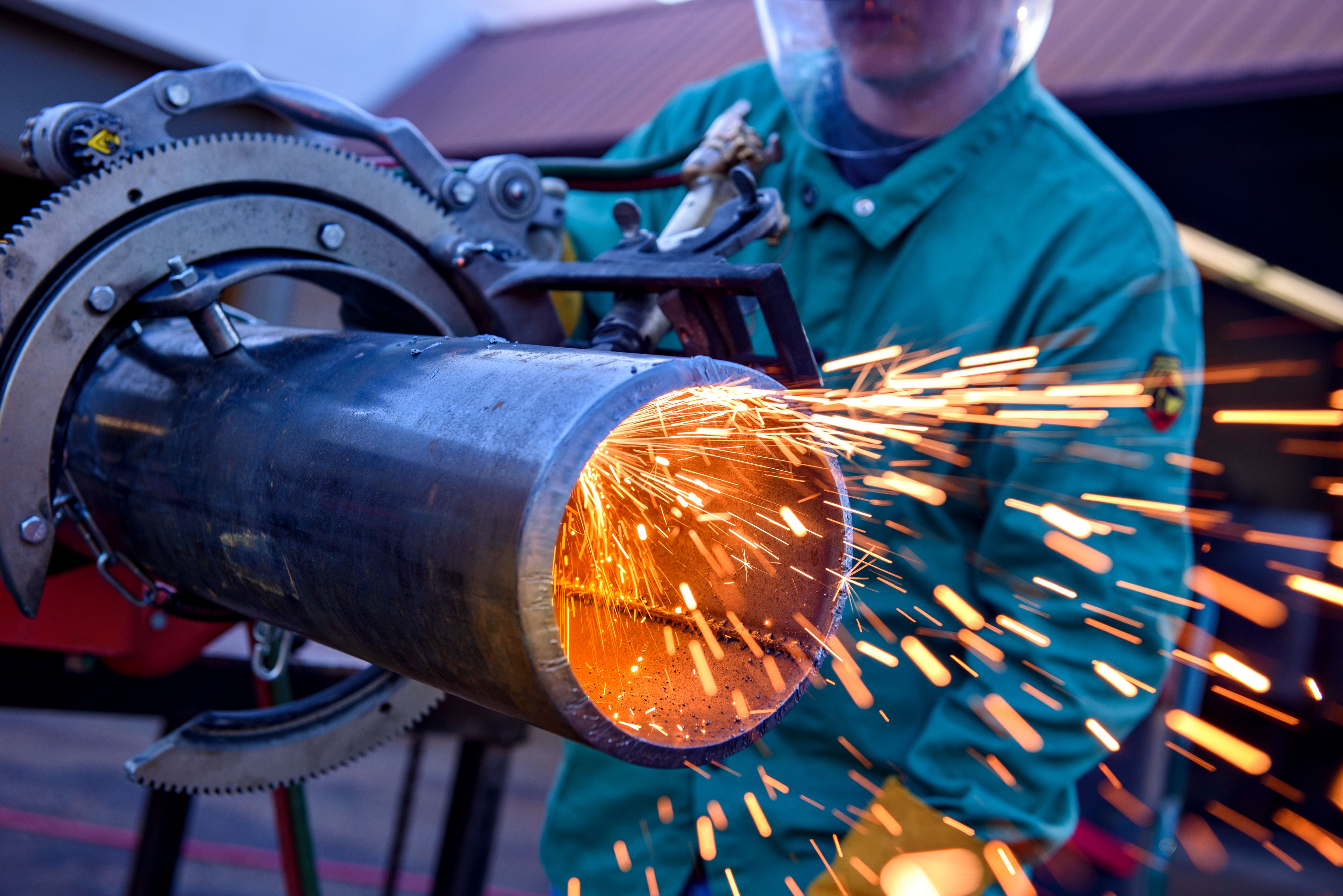 Image of a welder welding a pipe with orange sparks coming out one end.