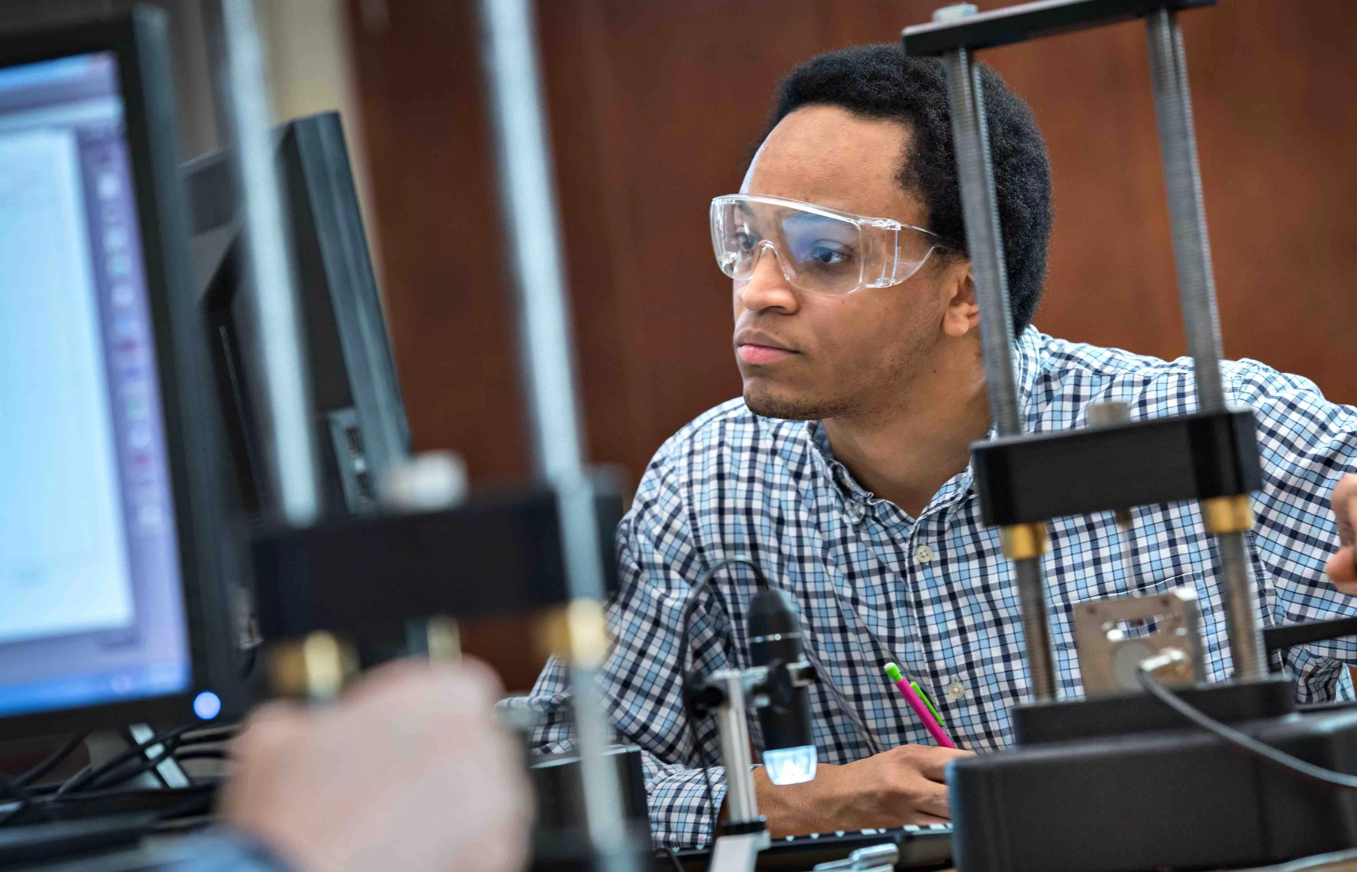 Man wearing safety goggles working on computer and taking notes